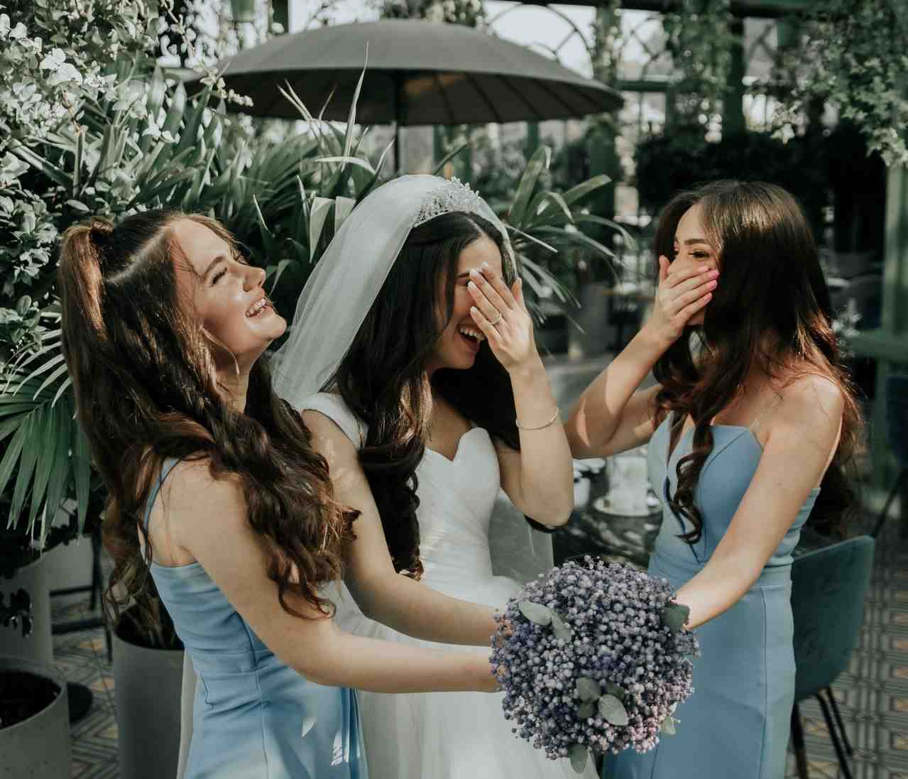 Bride holding flowers with bridesmaid and Maid of Honour either side of her. All of them are laughing
